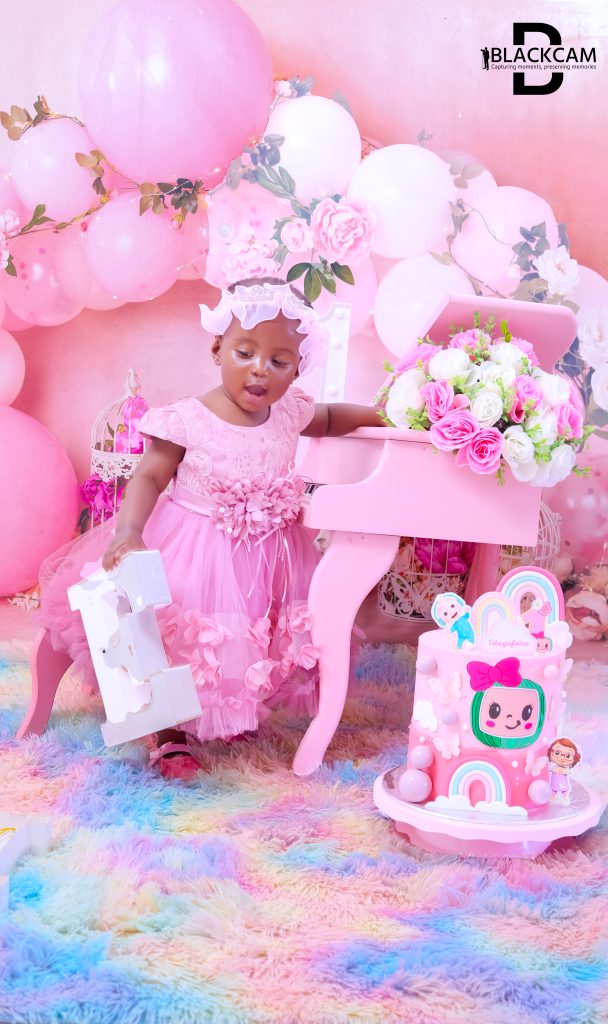 First birthday portrait in a bright pink studio setup with a miniature piano