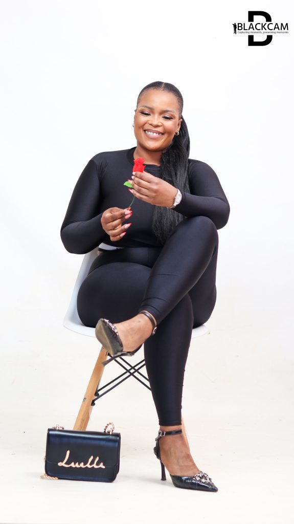 BlackCam studio portrait of a woman seated in a black outfit holding a red rose